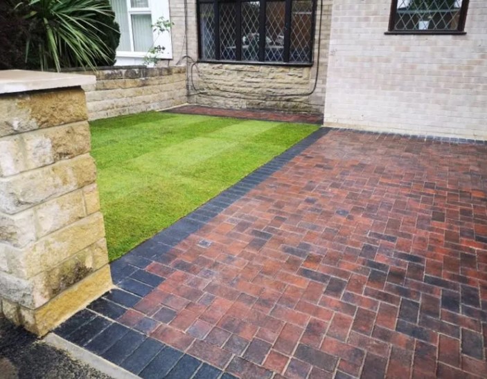 Warm red block paving with a dark edge beside fresh grass